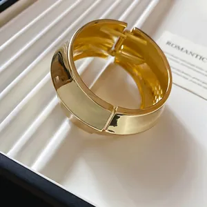 Minimalist gold wide wave bangle featuring a polished hinged design on a textured tray