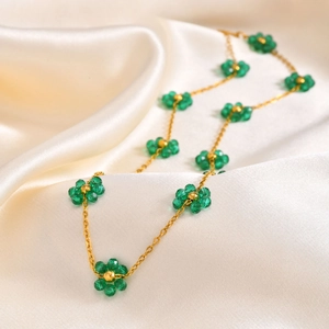 Detailed shot of emerald green flower necklace with gold chain on elegant white silk