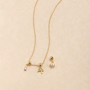 Detail of gold necklace with bow pendant, zircon stone bar and elegant pearl charms