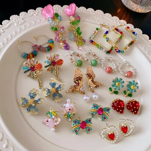 Detailaufnahme bunter Blumenohrringe und Perlenanhänger auf einem weißen Reliefteller