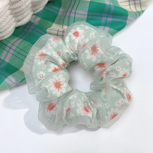 Close-up of green daisy pattern scrunchie with transparent mesh layer on white surface