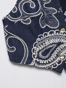 Detail of dark blue denim top with white embroidery and polished gold metal buttons