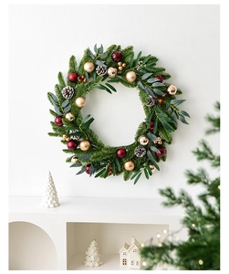 Close-up of Christmas wreath with pine needles, red ornaments and pine cones on white wall