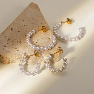 Detail view of C-shaped 18K gold stainless steel pearl earrings in two sizes on stone