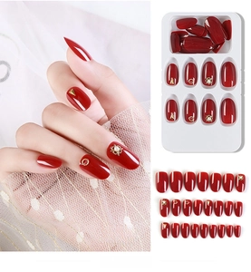 Detail of red press-on nails set with gold accents and faux pearls on white lace
