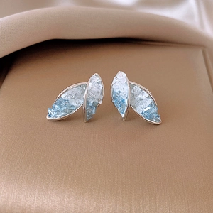Macro detail of silver feather earrings with gradient blue crystals on brushed gold surface