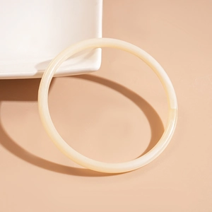 Top-down view of a minimalist round ivory acrylic bracelet on a beige textured surface
