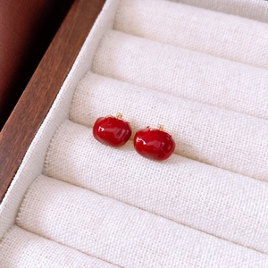 Macro shot of red enamel apple studs in a beige velvet jewelry box with gold accents