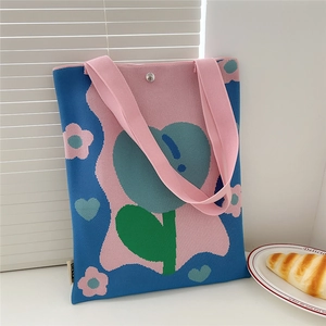 Detail of blue knitted tote bag with pink flower patterns and silver magnetic snap closure