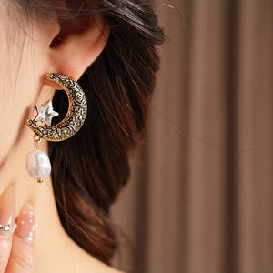 Close-up of vintage bronze moon and star earrings with baroque pearl on a model