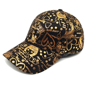 Detail of black baseball cap with gold graffiti pattern showing cartoon girl and texture