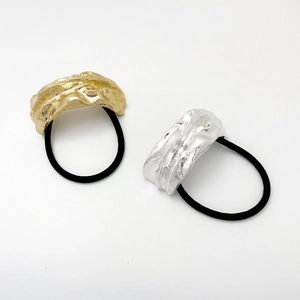 Detailed view of the irregular pleated gold and silver metal charms on black hair ties