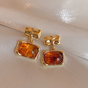 Close-up of vintage gold earrings with amber resin drop on soft silk background