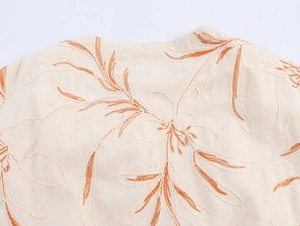 Macro detail of floral embroidery and cotton linen texture on an ivory bomber jacket