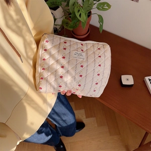 Floral quilted cosmetic bag in beige with red flowers, held in a cozy lifestyle setting