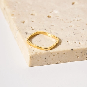 Minimalist square golden metal ring on a beige stone base with polished finish