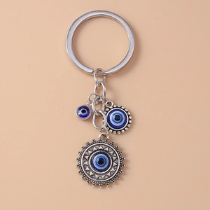 Detail of silver vintage sun palm evil eye keychain with blue charms on beige background