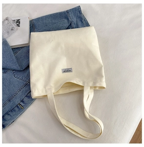 Detail of beige canvas tote bag with black Fashion Instinct label on white bedding