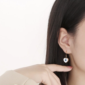 Close-up of heart-shaped evil eye earrings with gold hooks on model's ear