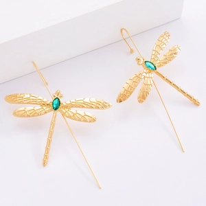 Détail de boucles d'oreilles libellule dorées avec gemme verte et ailes évidées