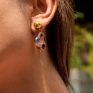 Gros plan d'une boucle d'oreille dorée avec pendentif translucide foncé sur un modèle