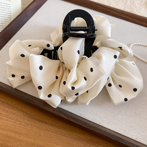 Detailed view of polka dot bow hair claw clip with cream satin fabric on a tray