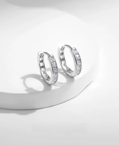 Macro detail of U-shaped silver hoop earrings with square zircon stones on a white stand
