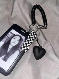 Detail of checkered heart pendant and black card holder with spring hook on gray fabric