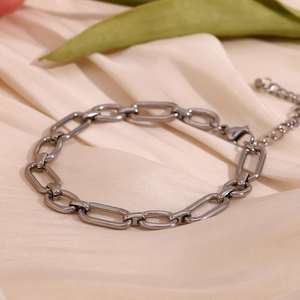 Close-up of a silver paperclip chain anklet with lobster clasp on beige silk fabric