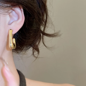 Close-up of a polished gold U-shaped earring showing high-gloss metallic texture on ear