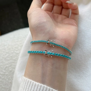 Close-up of stacked silver tennis bracelets with turquoise stones on a wrist