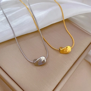 Gold and silver twisted bean pendant necklaces on sleek snake chains in a minimalist style