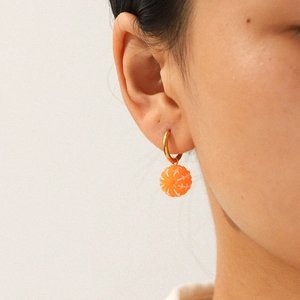 Chic gold hoop earrings with orange fruit pendant charm worn on a model's ear