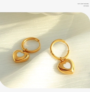 Detailed close-up of golden heart huggie earrings with white enamel on soft fabric