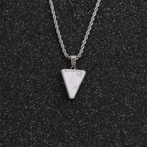 Détail d'une chaîne torsadée argentée avec pendentif triangulaire en marbre blanc sur fond sombre
