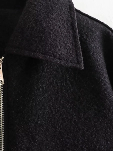 Detailed close-up of metallic zipper and soft fleece texture on black wool coat collar