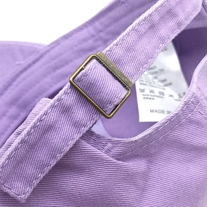 Detail of adjustable metal buckle and wash label on purple cotton baseball cap