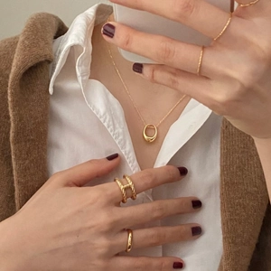 Detail of minimalist gold plated rings and oval necklace on a model wearing casual layers