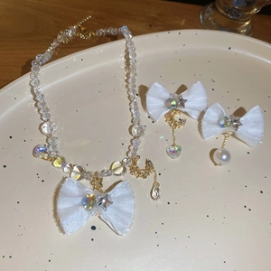 Detail of fabric bow jewelry set with crystal beads and moon charms on ceramic tray