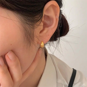 Close-up of golden shell-style ribbed earring on ear with fine vertical metal textures