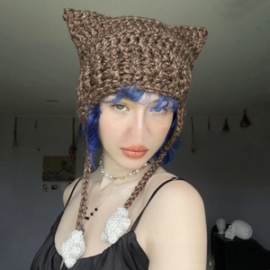 Close-up of brown crochet knit hat featuring cat ear design and white pom-pom braids