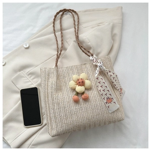 Close-up of woven straw tote bag texture with floral charm and white silk scarf