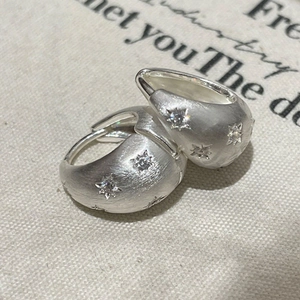 Macro detail of brushed silver star earring with zirconia on textured fabric background