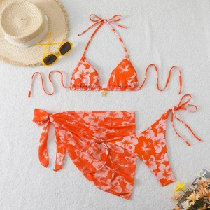 Detailed flat lay of a floral three-piece bikini set with matching sarong and summer props
