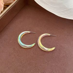 Macro view of iridescent acrylic C-shape hoop earrings on a velvet jewelry tray