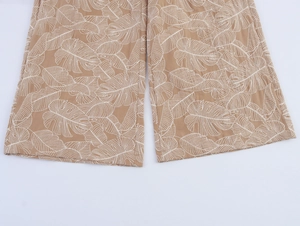 Detailed close-up of tan wide-leg pants featuring white tropical Monstera leaf embroidery