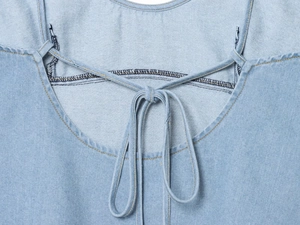 Detail der hellblauen Jeansstoff-Struktur mit einer Bindeschleife am Nackenband