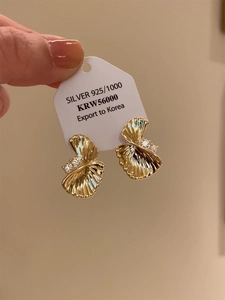 Detail of gold fan-shaped S925 silver earrings with ribbed texture and three clear zircons