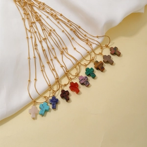 Cross necklaces with natural stone pendants and gold ball chains shown on white fabric
