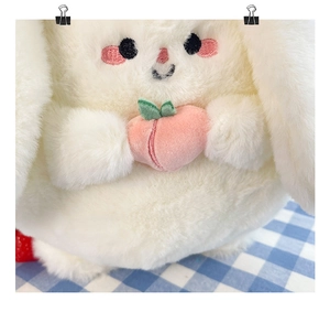 Close-up of white plush toy featuring a pink embroidered peach detail and soft texture